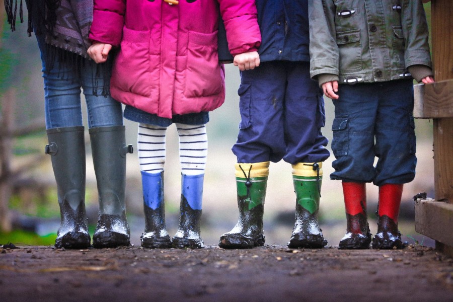 Fjögur börn sem standa hlið við hlið úti í náttúrunni í stígvélum. Sést ekki í andlit.