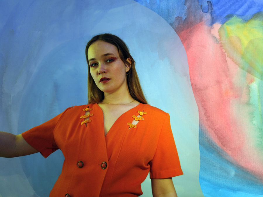 The musician Katrín Helga, also known as K.óla. She's wearing an orange shirt and the background looks like an abstract painting.