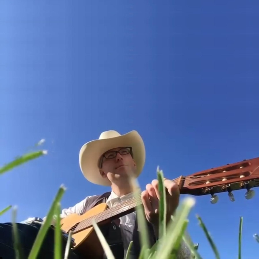 James Tristan Redding situr með gítar og kúrekahatt með bláan himinn í bakgrunni