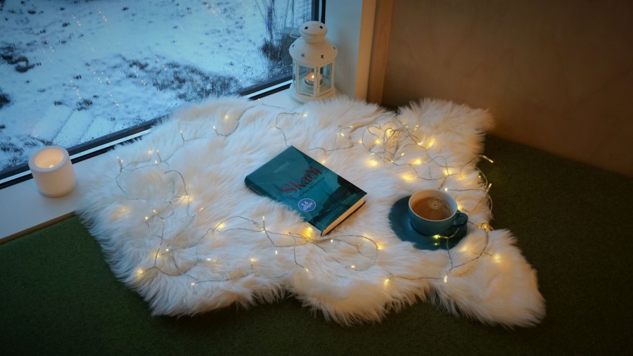 Hugguleg stemmning í glugganum á Borgarbókasafninu í Úlfarsárdal Bók, kaffibolla, kerti , lukt og ljósaseríu stillt upp á gæru úti í glugga.